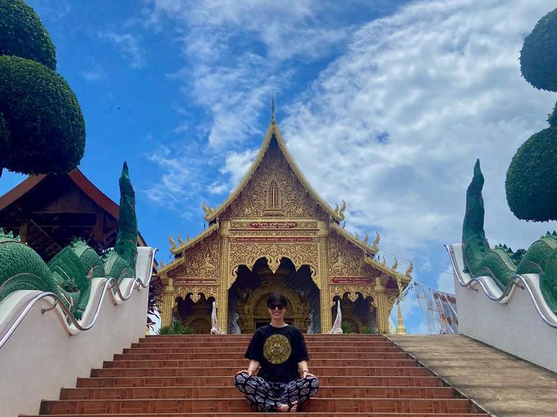 Woman sitting on steps from of a golden temple in Thailand