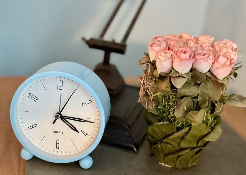Blue alarm clock with dried flowers on night stand