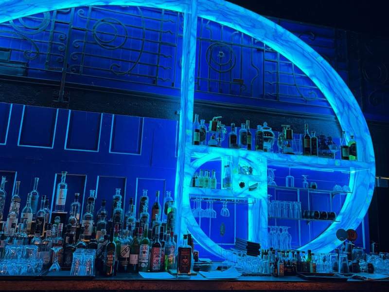 Neon blue back bar at Obscure Distillery in Los Angeles, with liquor bottles displayed against a dramatic glowing circular shelf. Photo credit: Kim Orlando