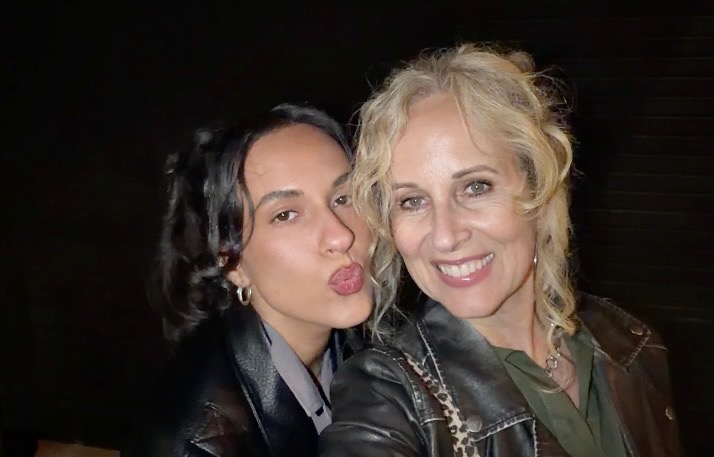 A mom and daughter posing together against a black background.