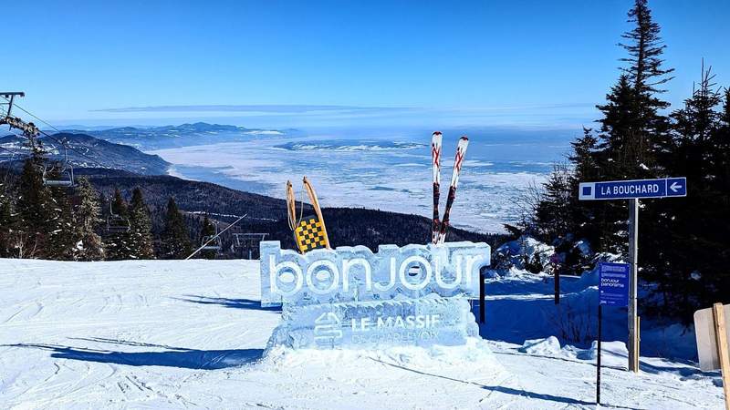 An ice sculpture sign saying bonjour with a view of the St. Lawrence River in the background at the summit of Le Massif at Club Med Charlevoix.