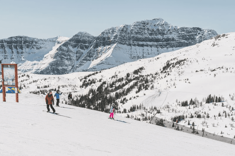 Family skiing with the Rocky Mountain peaks behind them at Banff Sunshine Village.