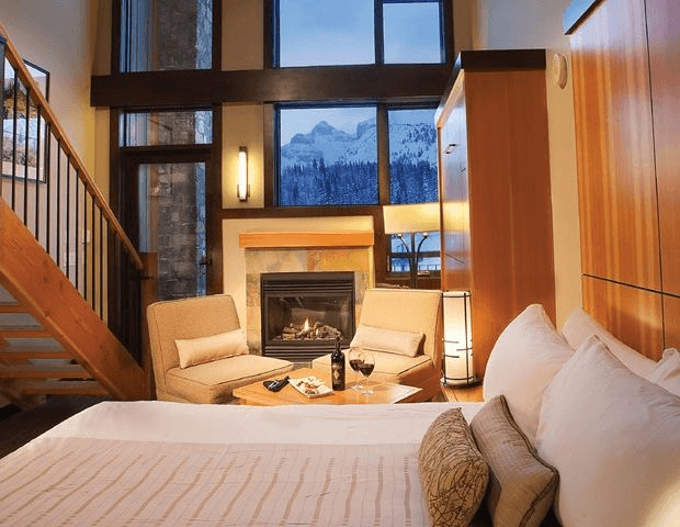 An interior shot of a luxury suite at the Sunshine Mountain Lodge with a fireplace and mountain view.