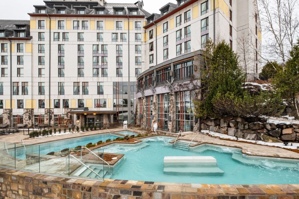 Exterior view of the Fairmont Tremblant Hotel and their large outdoor terrace with a heated pool and hot tubs.