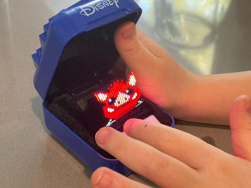 A young childs hand plays with a portable toy featuring the face of a Disney character.