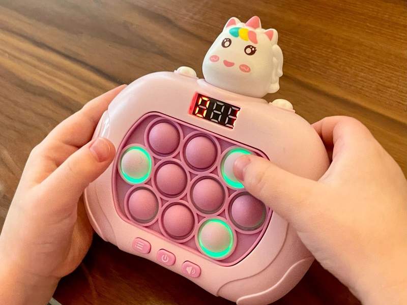 A childs hands play with a small pink toy with circles that light up.