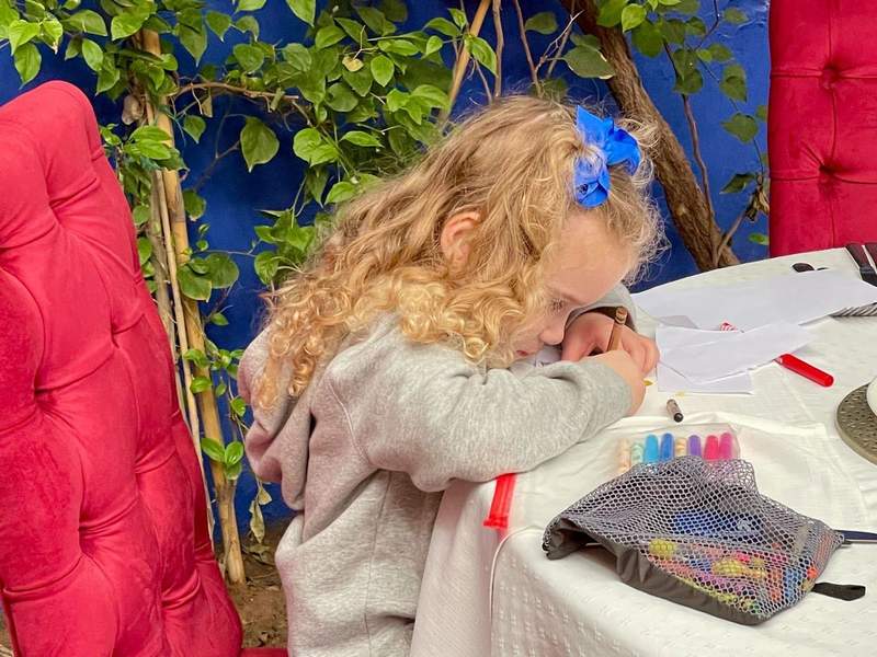 A young girl draws at a restaurant table using paper and crayons.