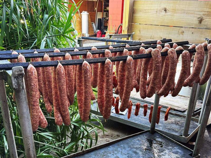 Authentic andouille sausages hanging outside on a rack at a smokehouse.