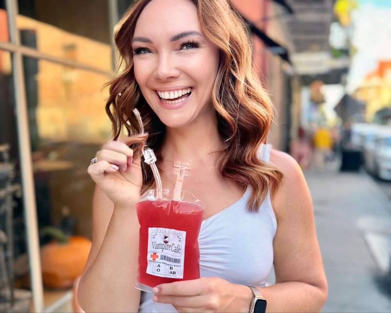 A woman smiling and holding a red drink in a blood bag from a bar in New Orleans. 
