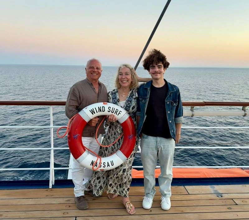 Family standing on deck of cruise ship with a life ring with ship name on it.