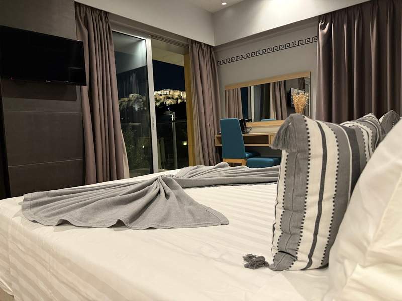Looking across a nice hotel room out the window at the Acropolis at night.