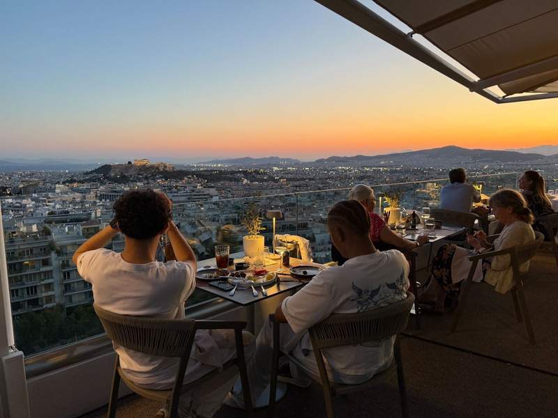 People sitting on a restaurant patio overlooking Athens at sunset.