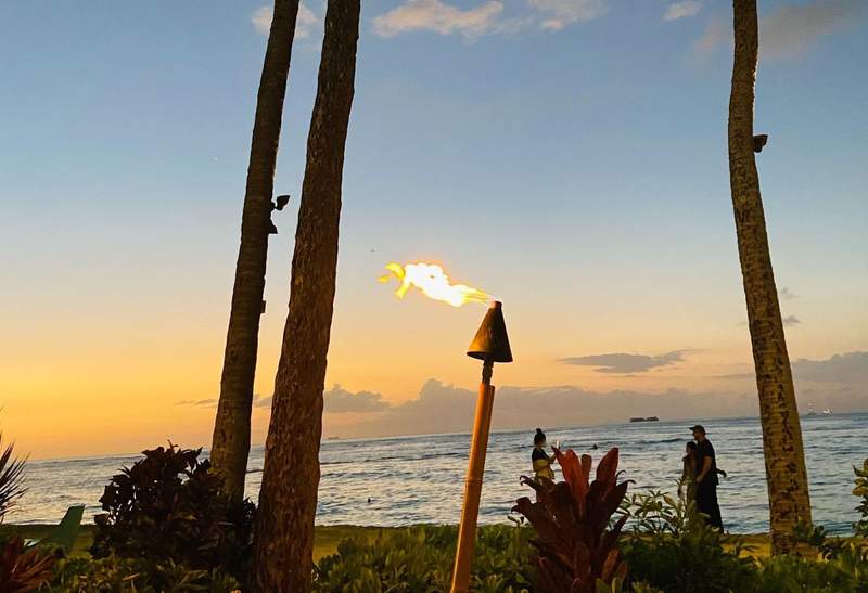 A tiki torch burns on the beach in Hawaii as the sun sets.