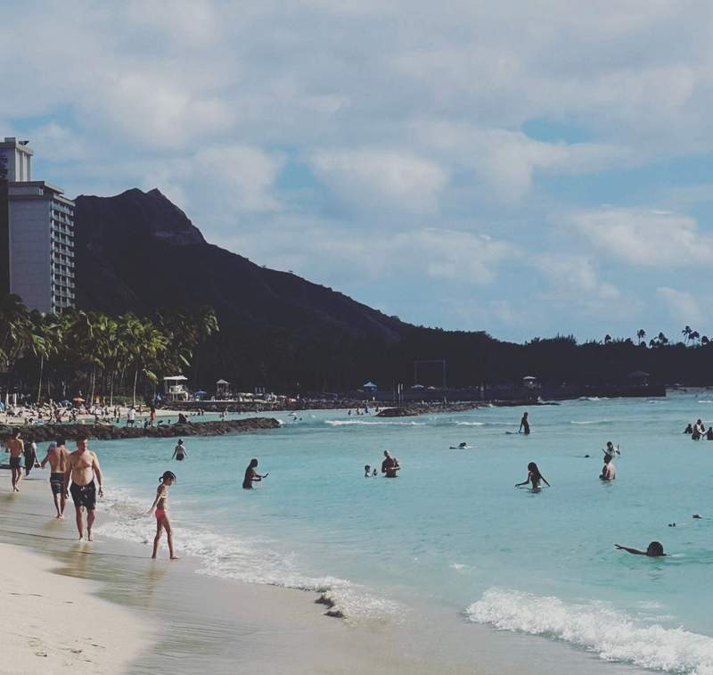 A crowd of beach goers enjoying Waikiki Beach with a view of Diamondhead in the background.