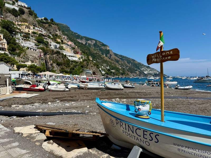 Looking over a beached small boat with a Welcome to Positano sign in it and the town and coast in the background.
