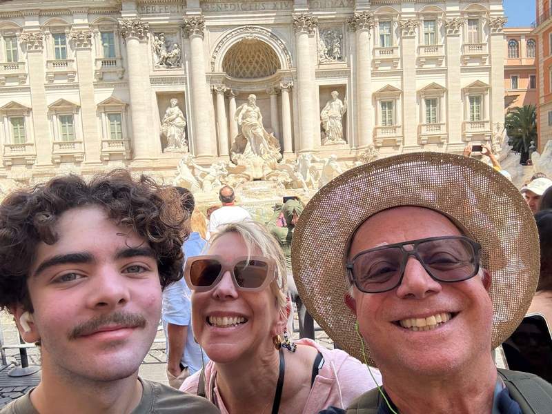 Smiling family in front of Trevi Fountain in Rome.