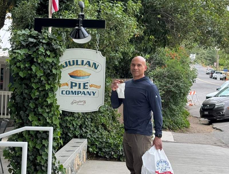 Man standing by a pie company sign holding a bag of apple treats