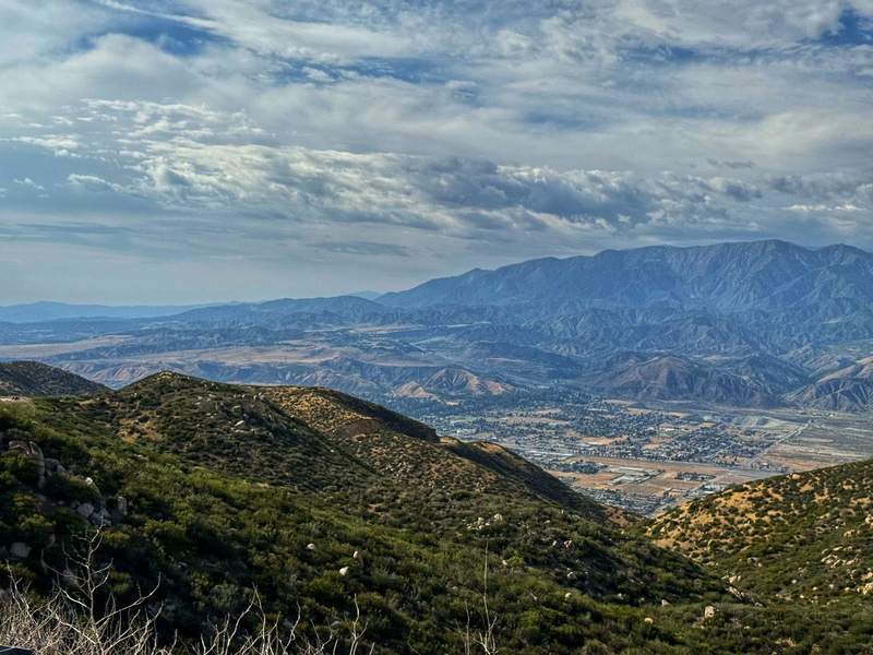 Mountains in shades of green and blue with a glimpse of the city of Palm Springs below