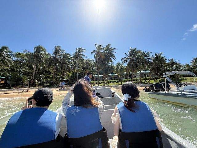Three passengers sit in a boat waiting to be transported from an island.