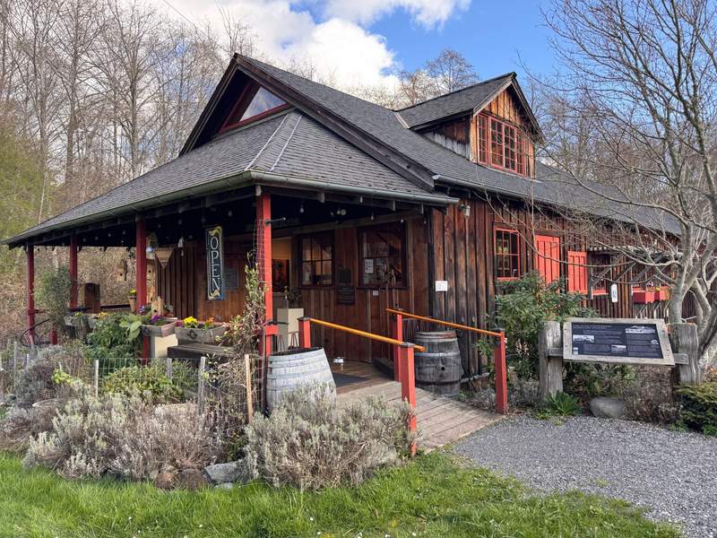 Alt text: Restored historic building with gables, a front porch with barrels and an interpretive sign about the history.