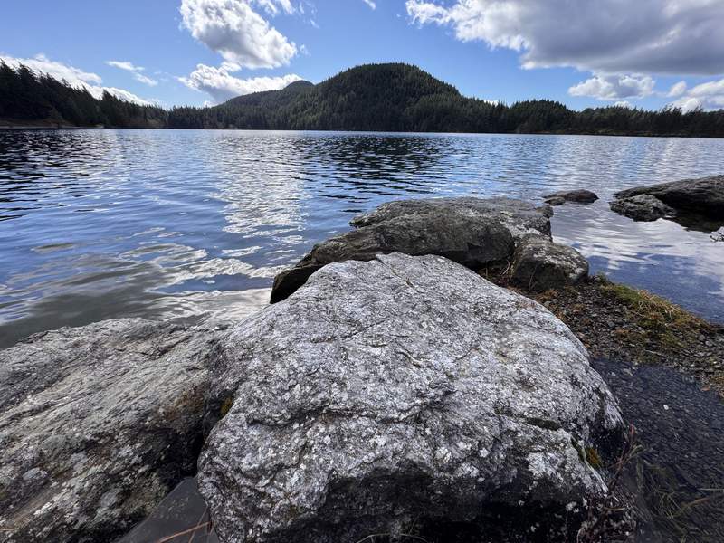 Alt text: Cascades Lake with hills in the distance and a rocky beach in the foreground.