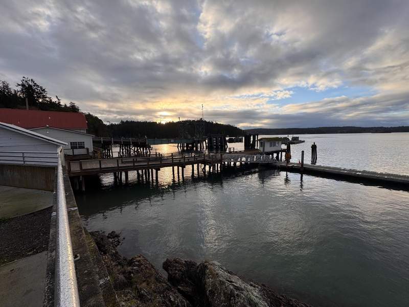 Orcas Island Ferry Terminal at sunrise shows the terminal building and ferry dock with the sun rising in the distance.