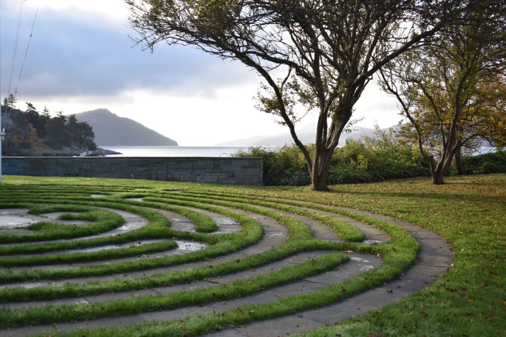 A grass and stone labyrinth overlooks a bay with islands in the distance