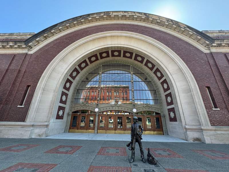 Large building with an arch with windows that reflect downtown Tacoma, in front a statue of a man and a dog.