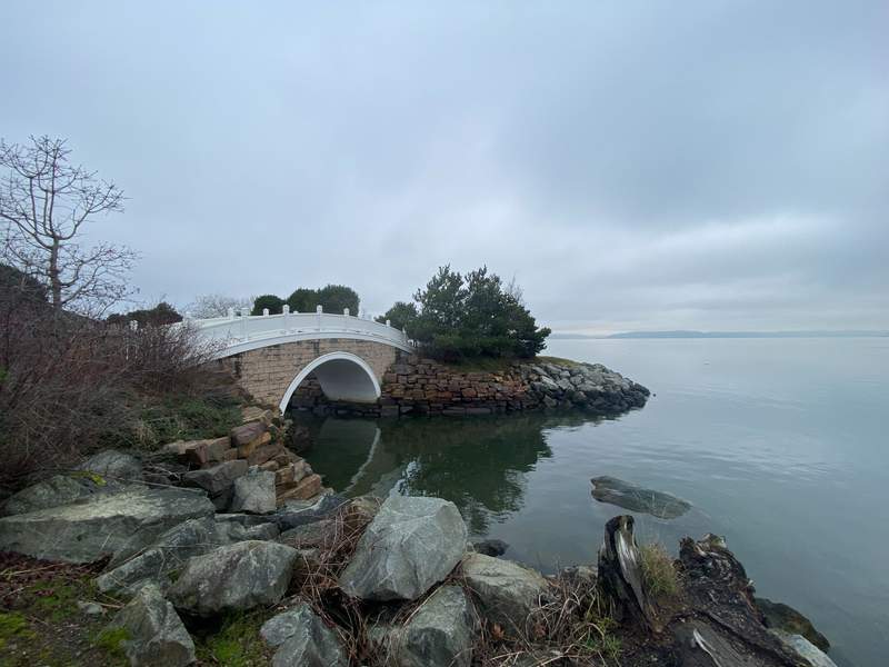 Waterfront with an ornamental bridge with rocks along the water in a park.