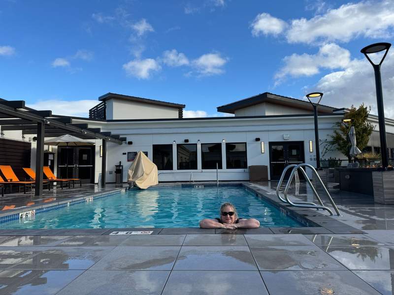 Girl in a swimming pool. The pool deck has orange lounge chairs.