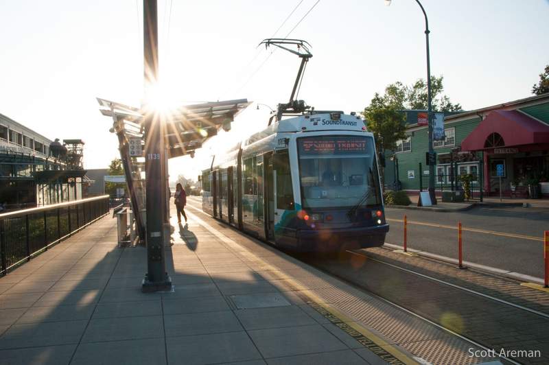 Link rail train pulls into a station next to a street.