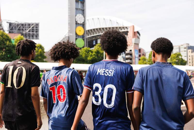 Four fans wearing soccer jerseys head to a soccer match. Lumen Field stadium in the distance.
