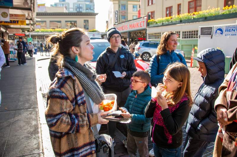 A group of people gathered around a sample container during a food walking tour