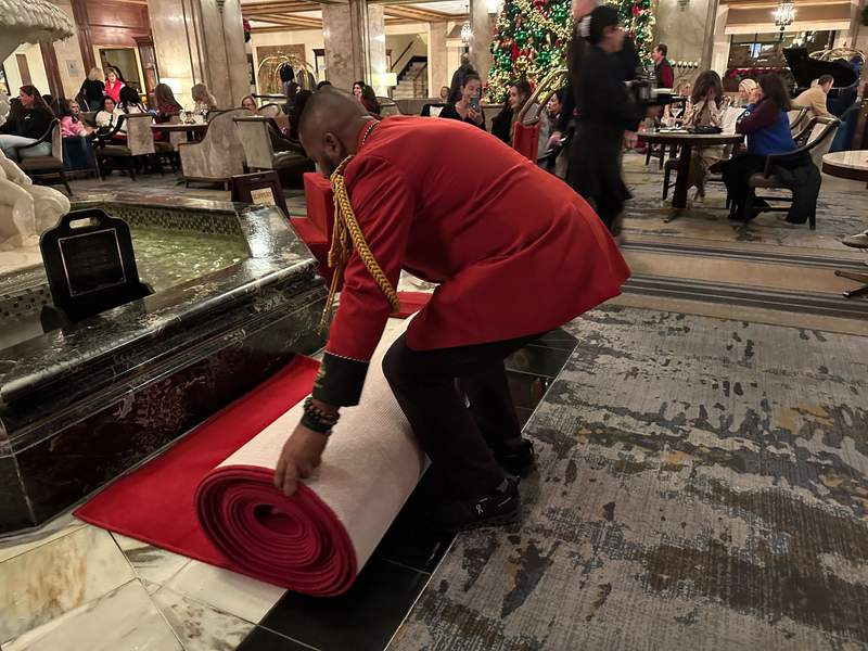 A man in a red jacket unrolling the red carpet. 