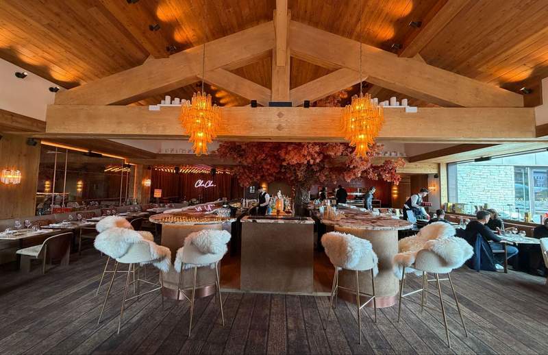 Interior of ChaCha restaurant at Residence 1850 bar with large decorative tree and pink foliage fur draped bar stools with gold legs chandeliers and exposed wooden beam cathedral ceilings