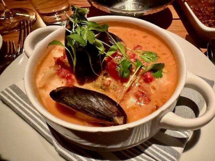 Colorful coastal seafood stew in a white bowl topped with mussels