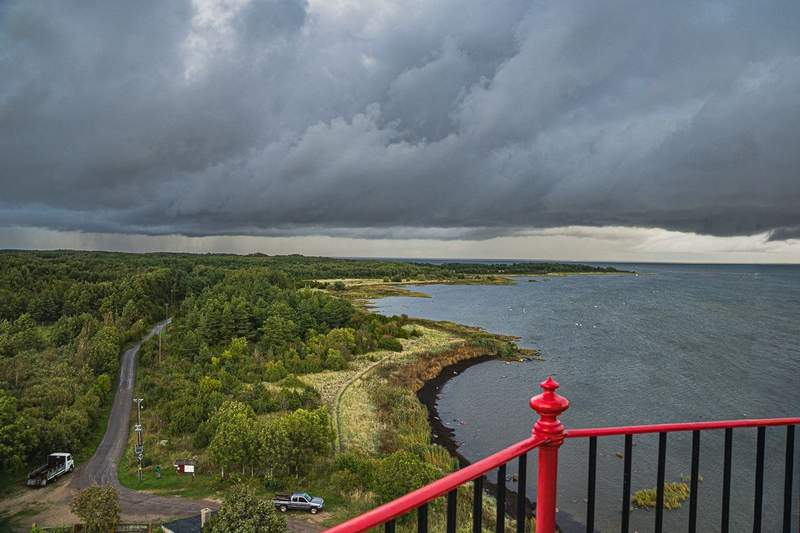 A small section of red railings around the lighthouse deck and looking down on the Kihnu coastline with heavy dark storm clouds on the horizon