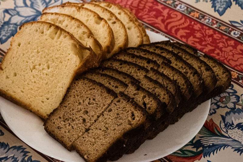 A white plate with slices of white bread and a dark brown bread. The dark bread slices are cut in half. The plate is resting on a colorful table cloth.