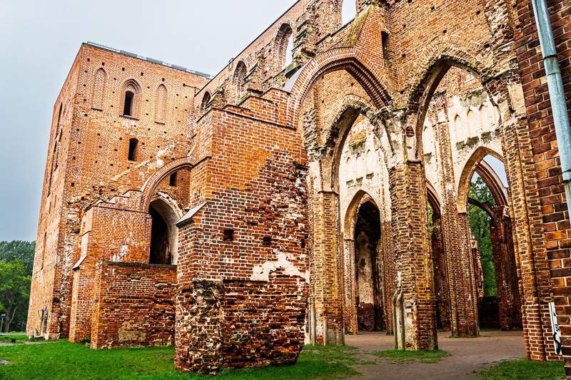 A red brick tower, buttress and archways of a roofless structure that was once a cathedral. 