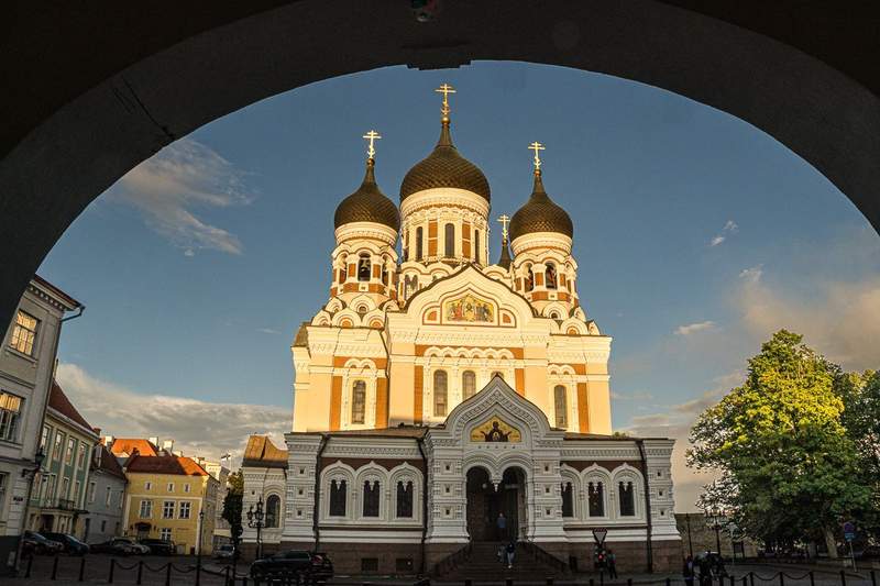 Alexander Nevsky Cathedral with three onion domes lit by the warm afternoon sun and frames by an archway.