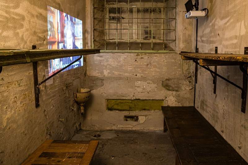 cell that housed prisoners in the KGB detention center. beds are planks bolted to whitewashed walls and there is a barred window that was blacked out.