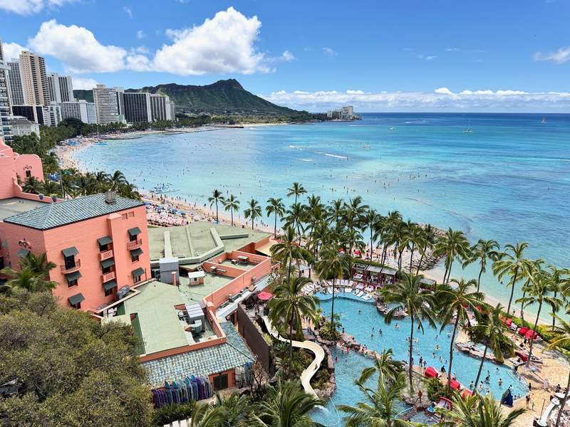 View from the 12th floor overlooking the ocean, Diamond Head in the background, the family pool and the beach lined with palm trees.