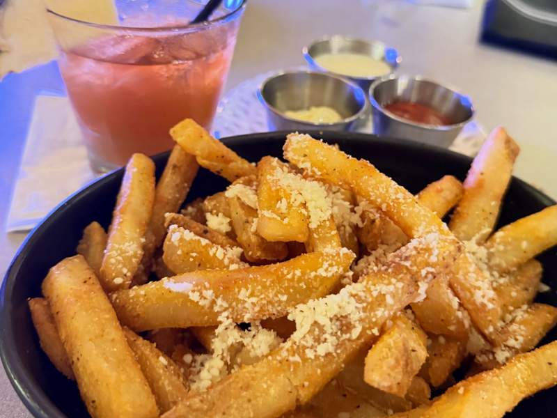 Close up of delicious crunchy french fries topped with truffle and parmesan and dipping sauces in the back at RumFire Sheraton Waikiki. 