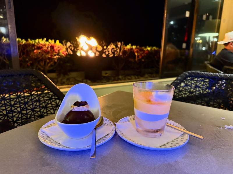 Chocolate dessert and mango cream dessert backlit by a firepit.