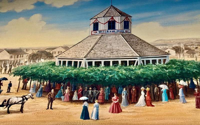 Color painting of eight sided building from 1847 surrounded by women in long dresses, hats and many with parasols. Green trees fill the space between the women and the building.