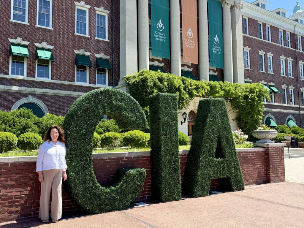 Woman in front of the exterior of a brick building on the Culinary Institute of America campus in Hyde Park, NY
