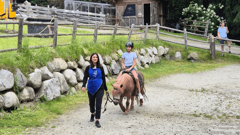 A young girl rides a pony, led by a staff member