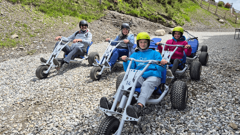 A group of four, including adults and teens, ride oversize  mountain tricycles on a gravel road.  