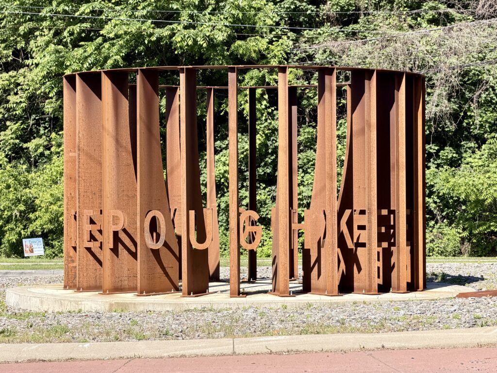 Circular, rust-colored metal sculpture with "Poughkeepsie" spelled out
