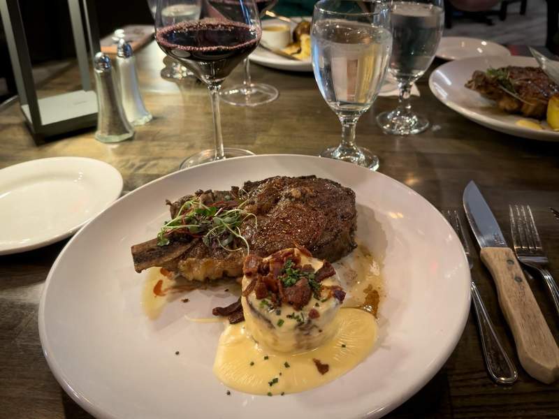 Steak dinner plated with sauce and vegetables beside a glass of red wine at Julieannas Steak and  Seafood.